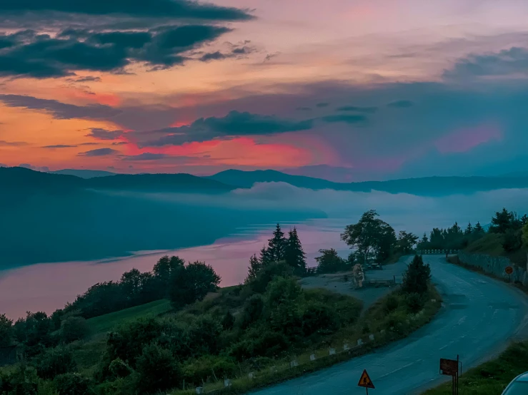 a highway surrounded by trees under a sky filled with clouds