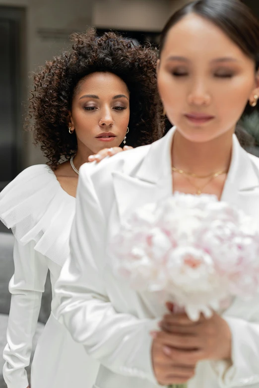 two women in dresses with one looking at the flower bouquet