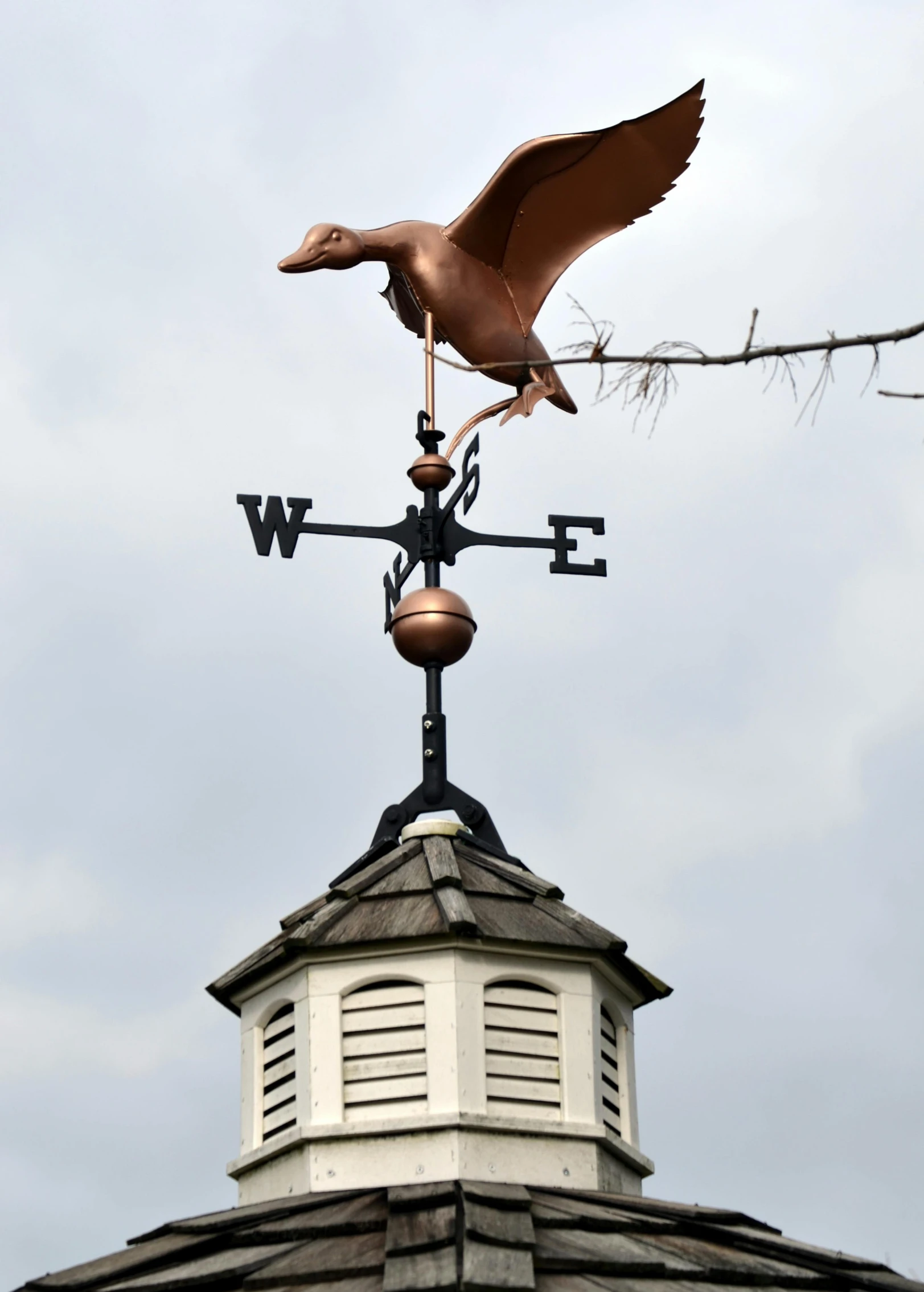 a weather vane on top of a building and a bird flying towards it