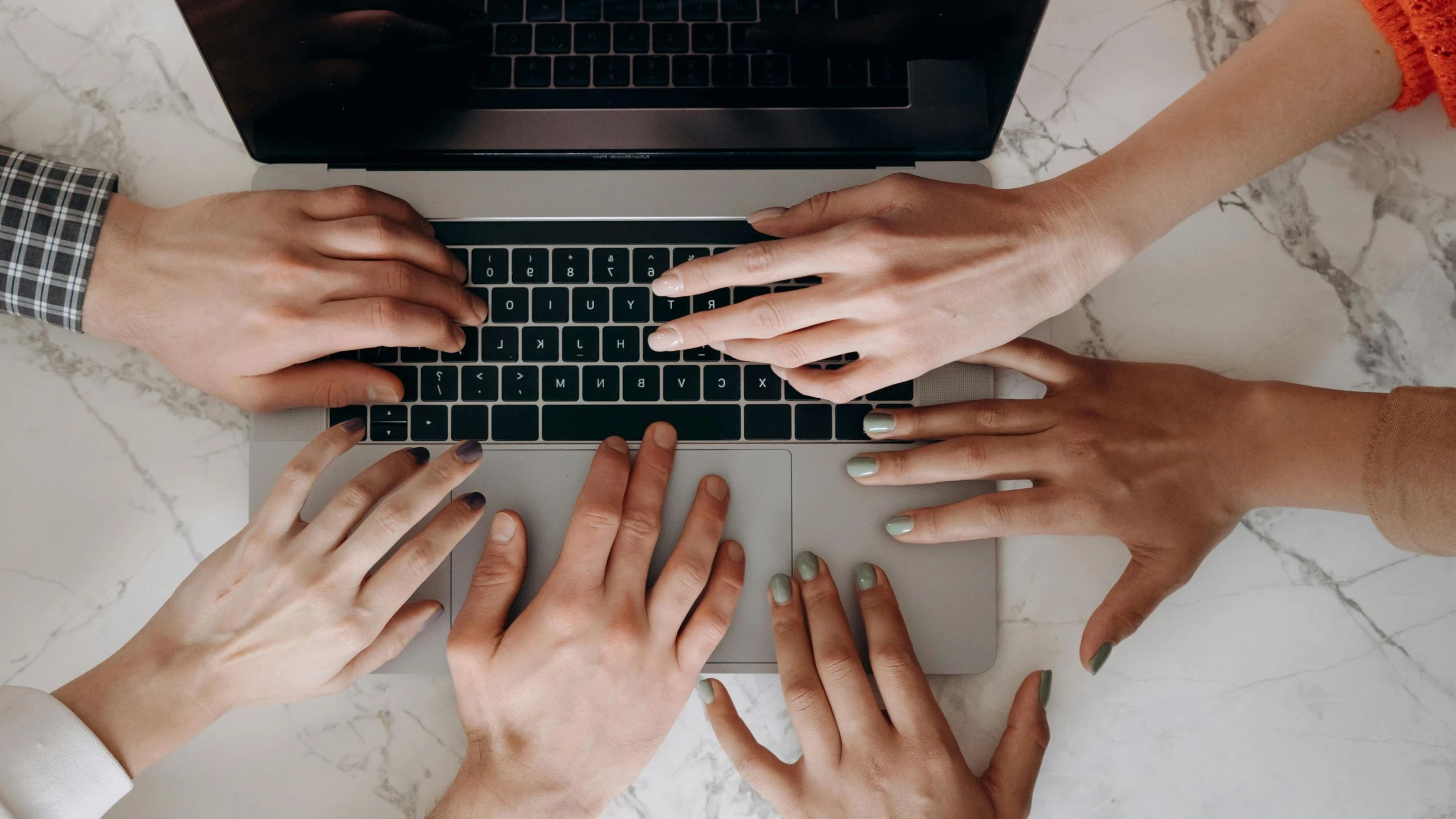 four hands typing on a keyboard together