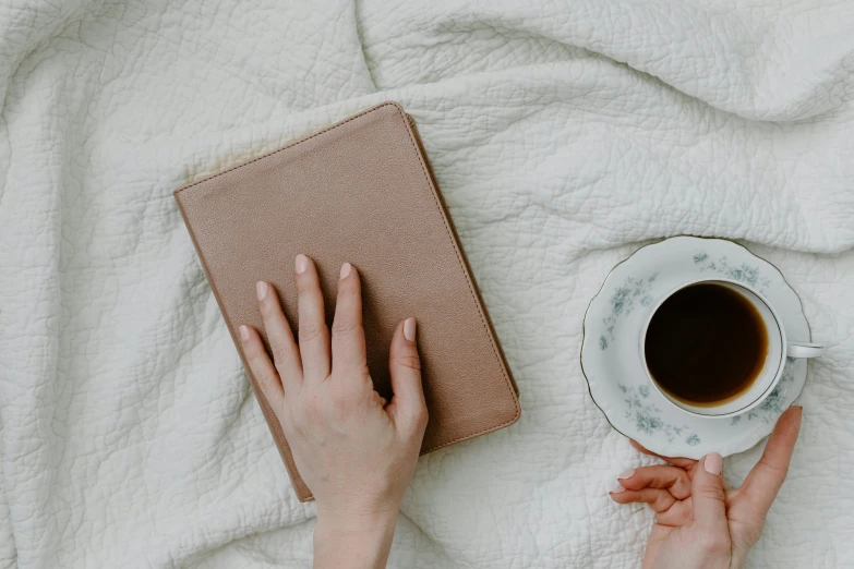 someone using their hands to hold a book and coffee