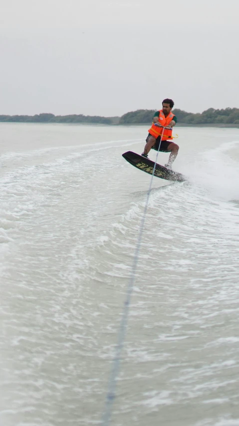 a man wearing an orange vest waterskiing on calm water