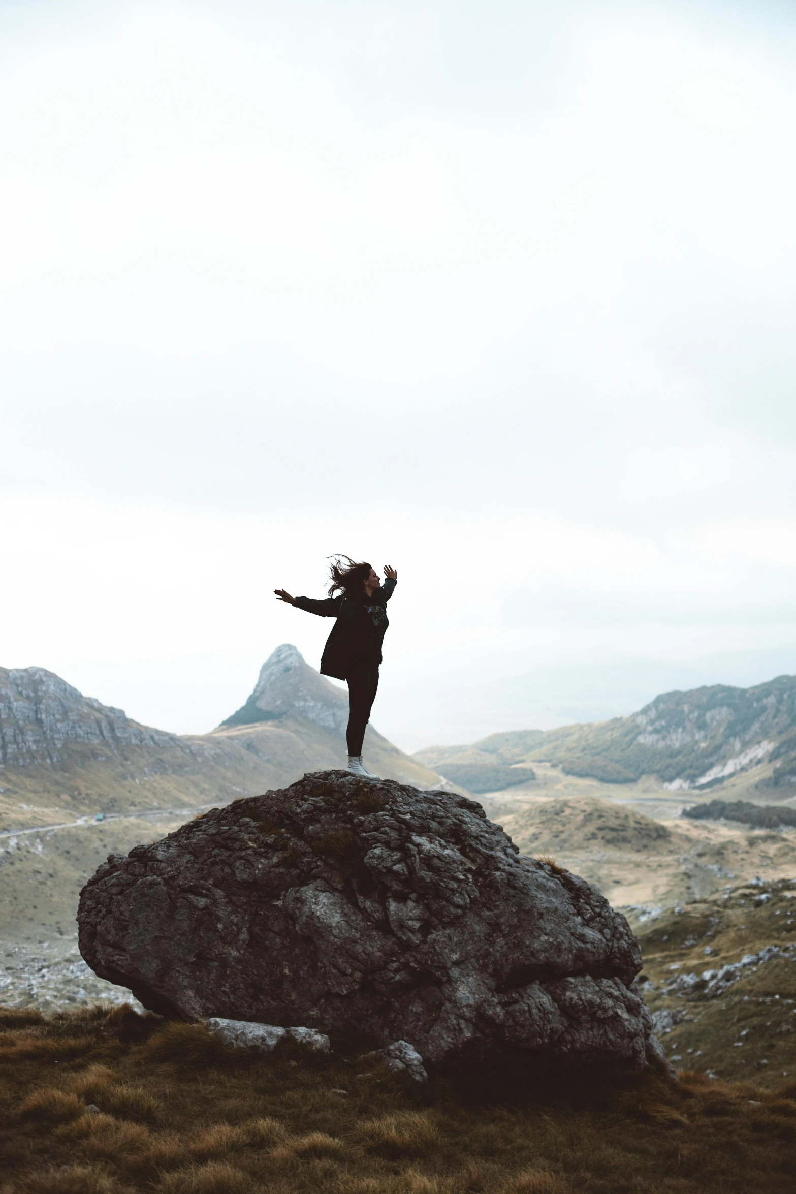 a woman with a coat and backpack standing on top of a rock