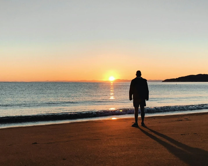 person standing on the beach as sun sets
