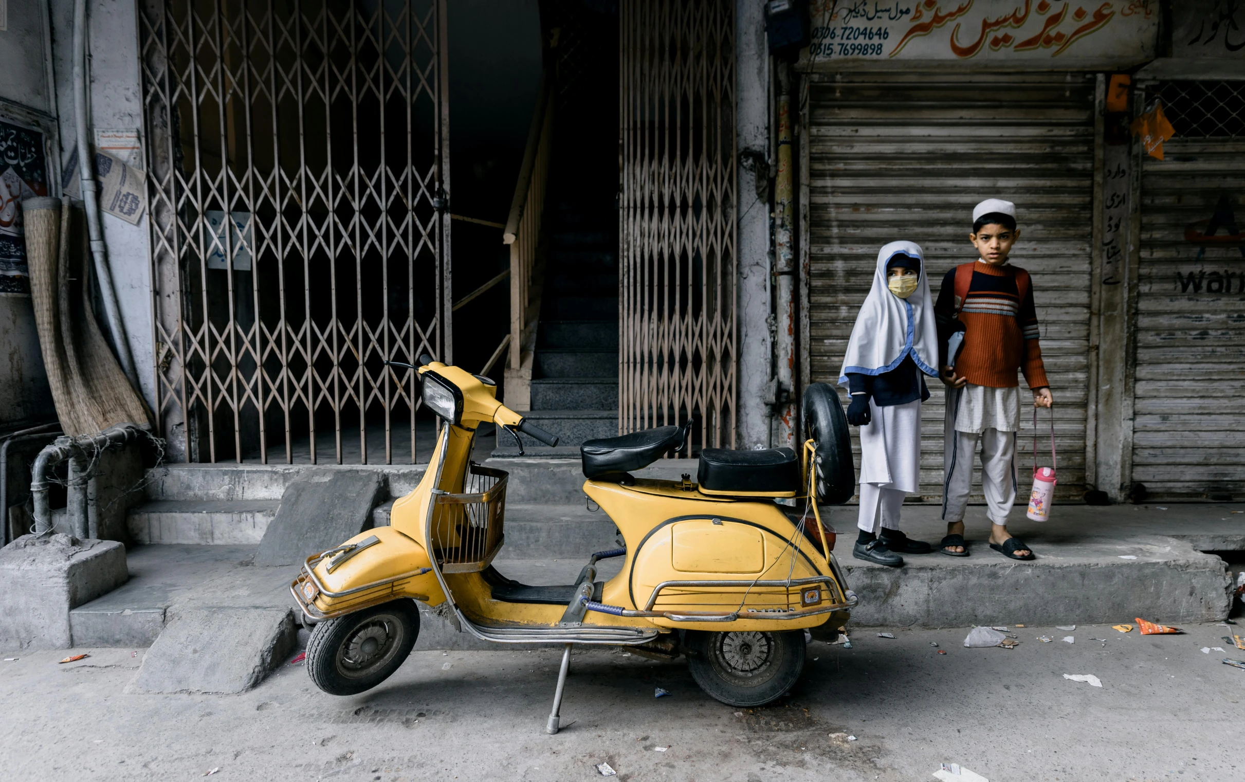 a little boy standing by his moped in front of a shop