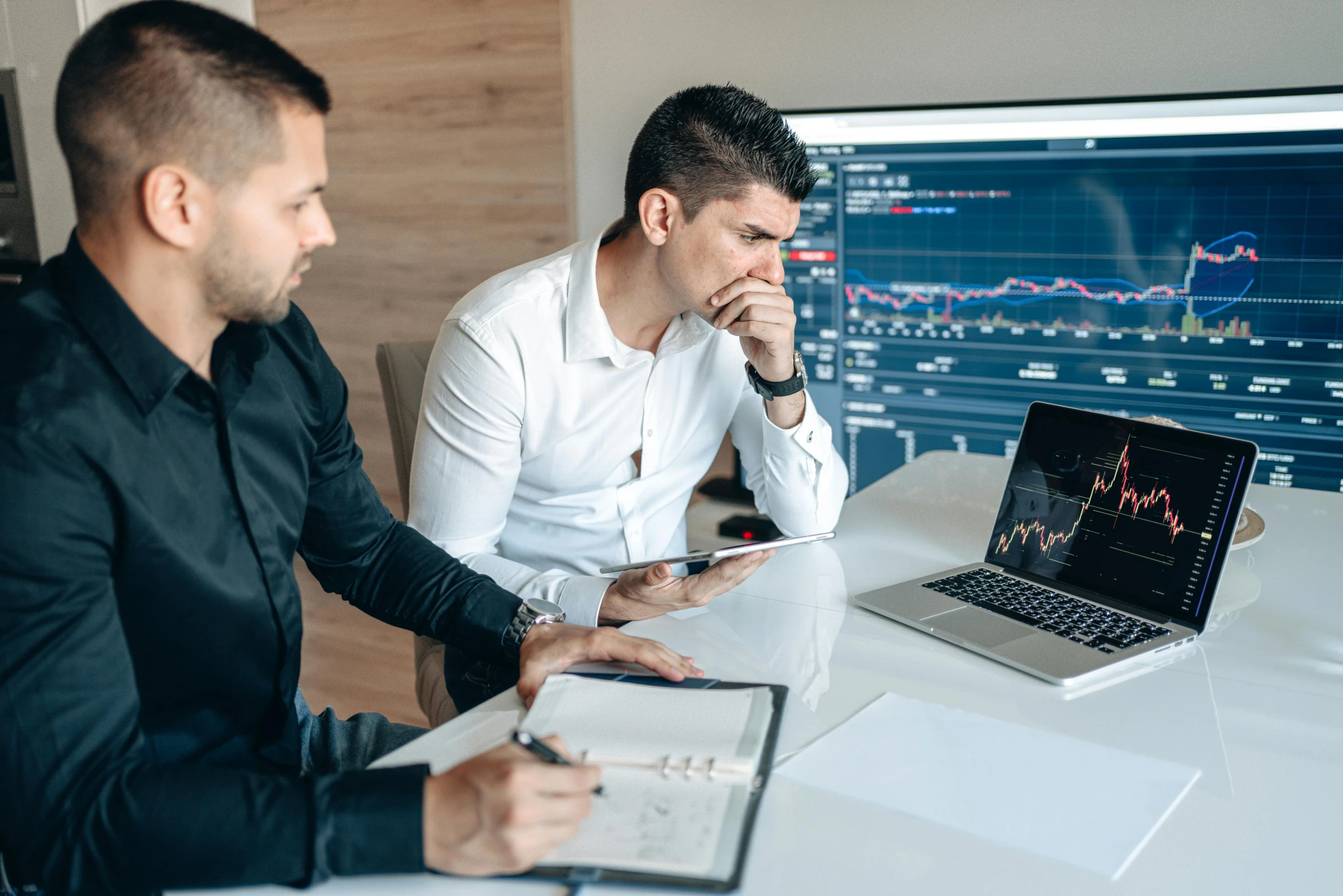 two men looking at a laptop and an ipad