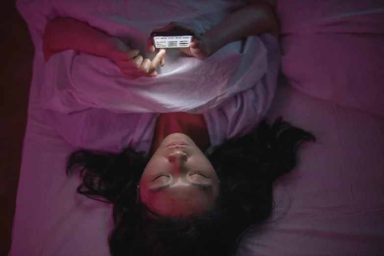 girl laying down on bed and holding up a remote