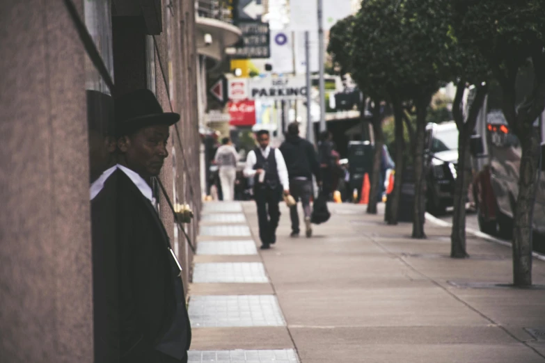 the side of a building on a street, where a man walks in a coat and top hat