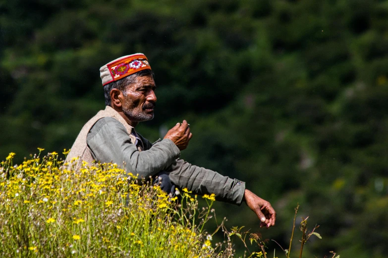 man with a red bandana on his head sitting in a field