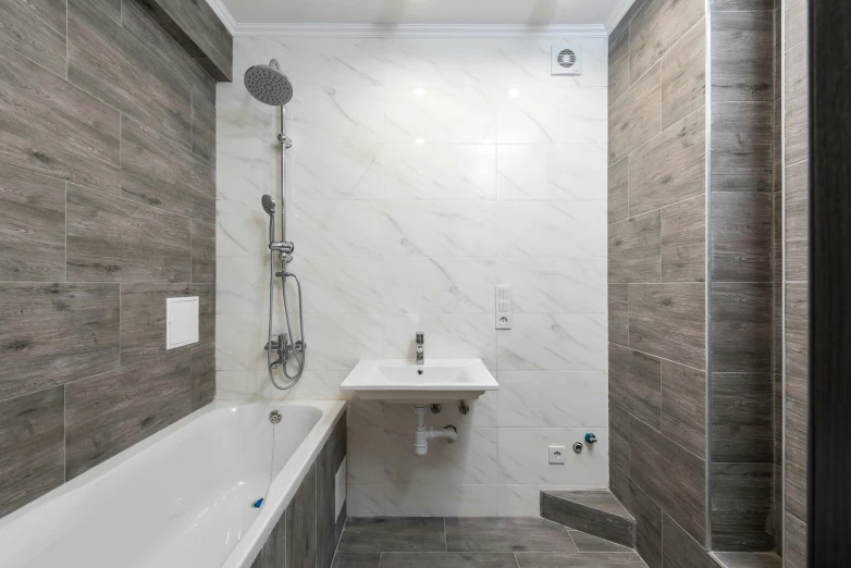 a bathroom with grey tile walls and a white bathtub and a sink