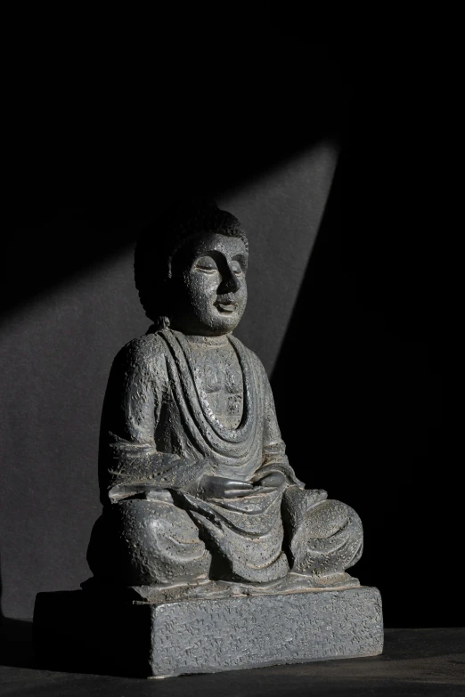 buddha statue sits in the dark light at the foot of a building