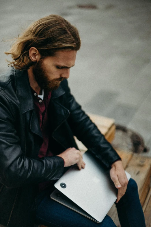 man with long hair sitting on bench with laptop in hand