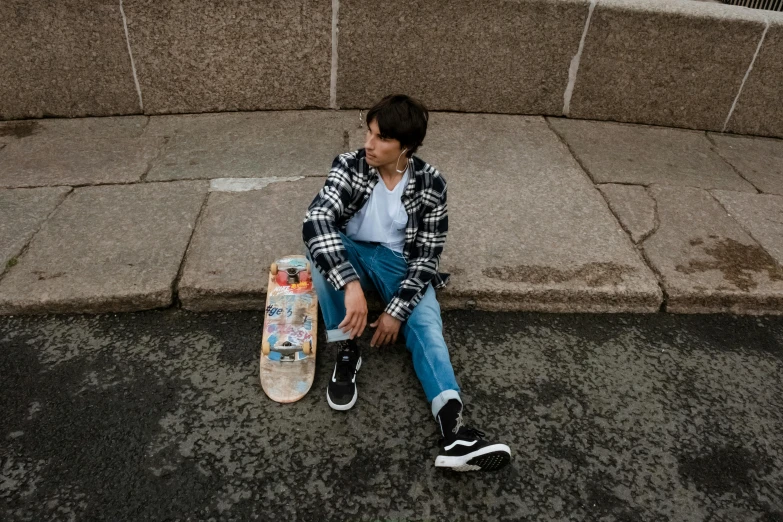a skateboarder sits on the curb with his board