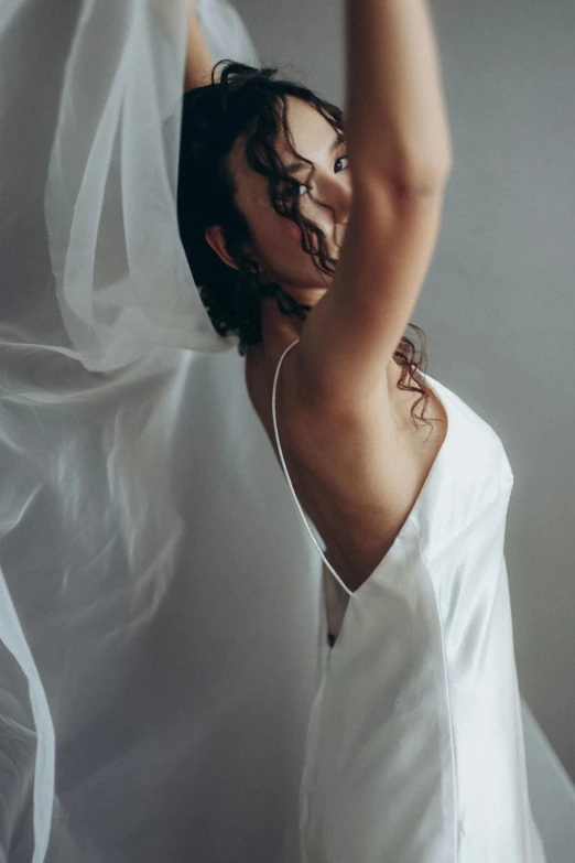 a woman in a white top and dress is holding her hands to the ceiling