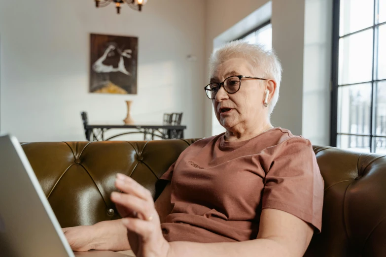 a woman in glasses uses a laptop while sitting on a couch