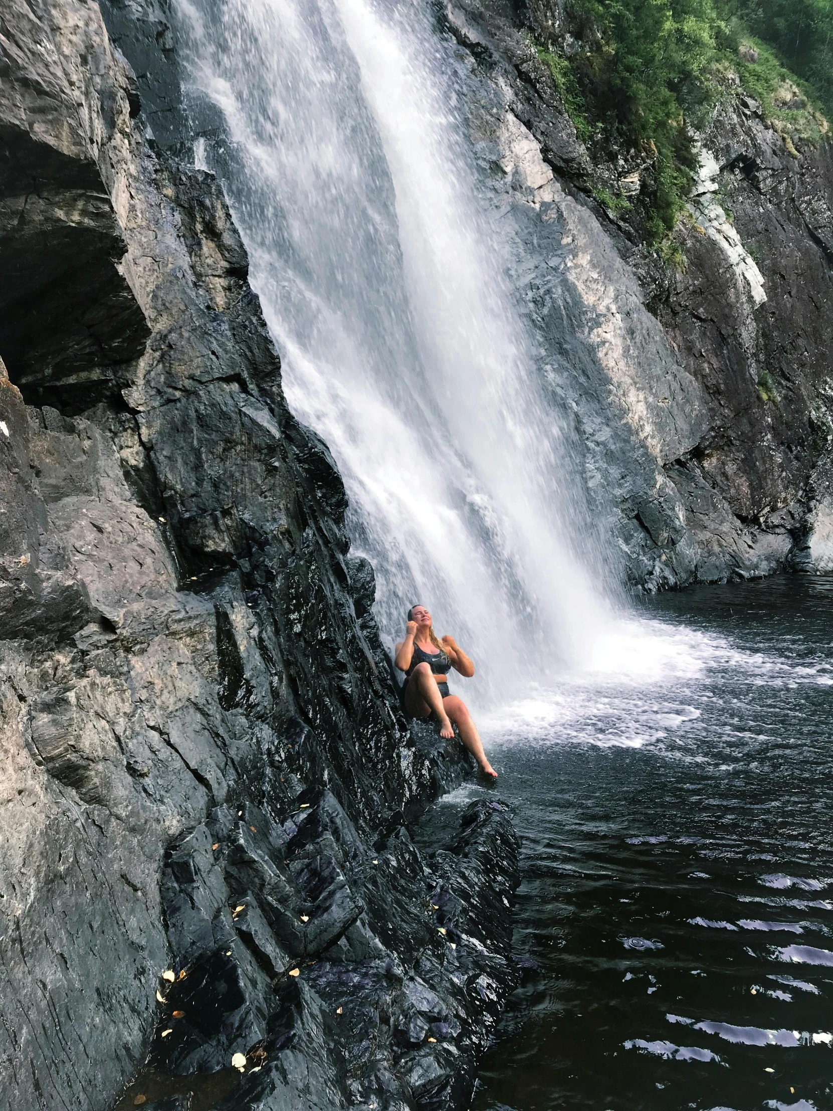 a man sitting on a cliff near the side of a waterfall