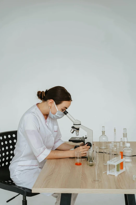 a girl wearing a white lab coat sitting at a table looking at soing