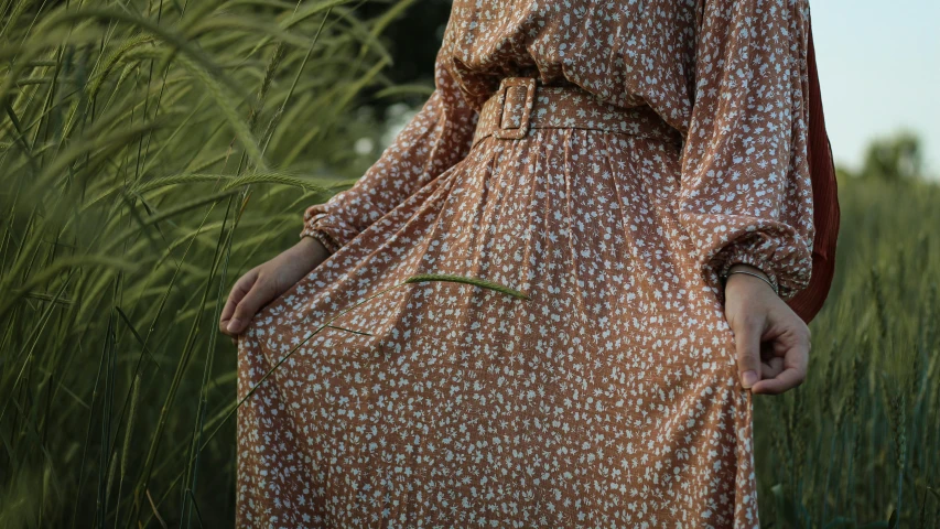 a woman is standing in a field, wearing a brown dress