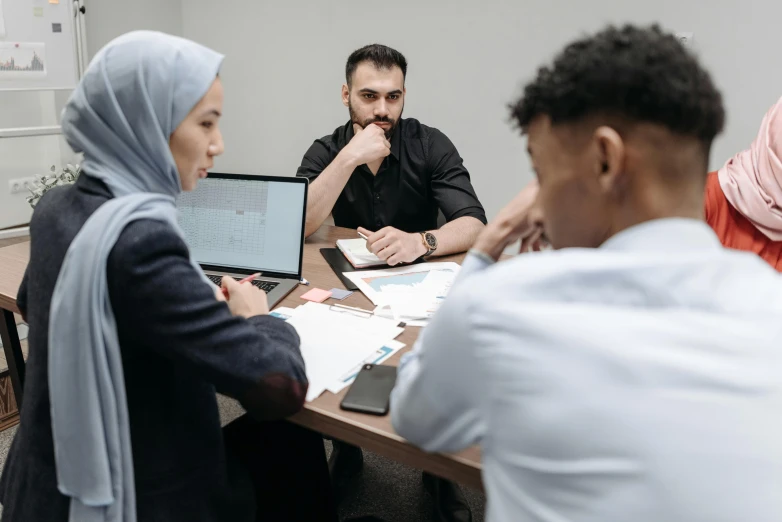 four people are sitting around a table using laptop computers