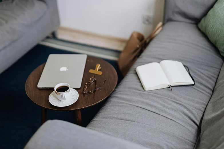 a gray couch with coffee, book, and a laptop on it