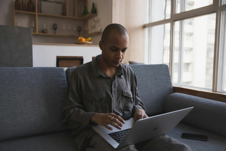 a man sits on a couch and uses a laptop