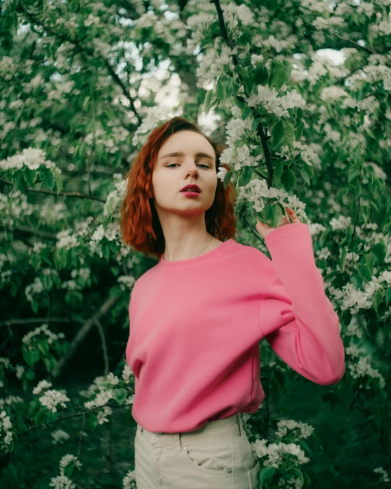 red headed woman in a pink shirt posing with green foliage behind her