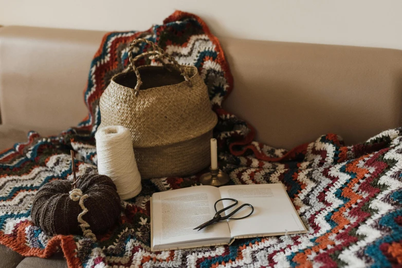 a book, crocheted afghan, scissors, and yarn on the bed