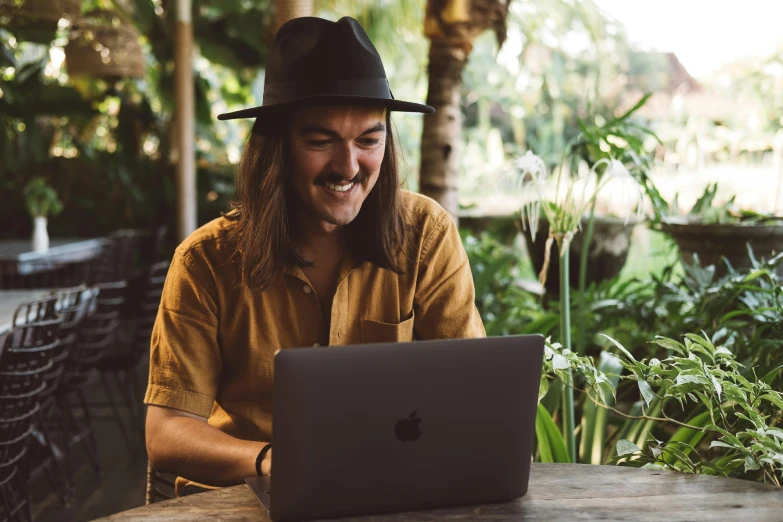 a person in a hat and yellow shirt on his laptop