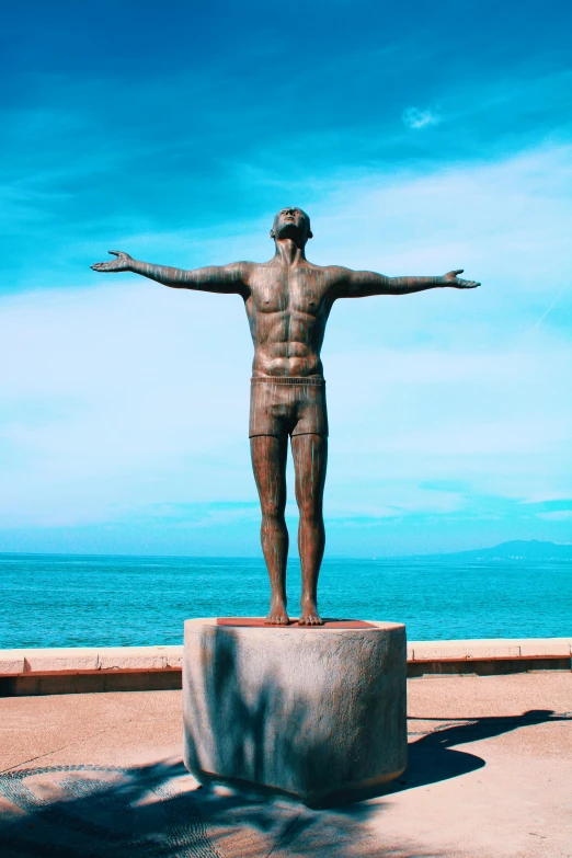 a statue of the man with his arms outstretched standing next to a large body of water