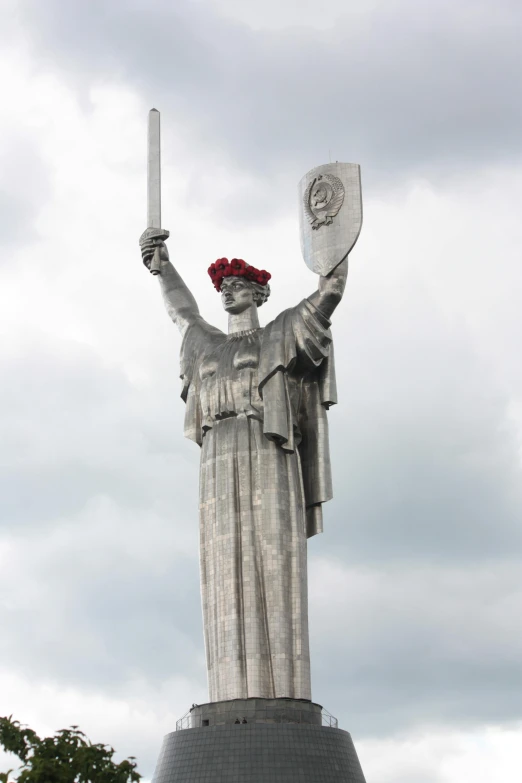 a lady with a rose hat holding a pair of scissors next to the base of a statue
