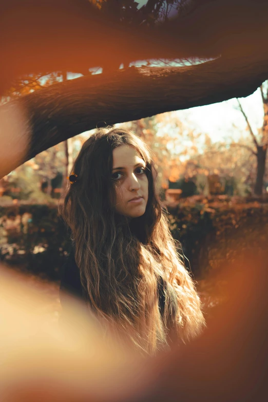 a young woman standing under a tree with long hair