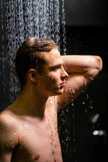 a man standing in a shower looking at the water from the faucet