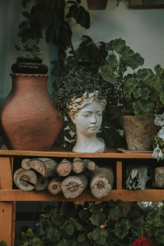 a collection of pottery on display with flowers, plants and a statue head