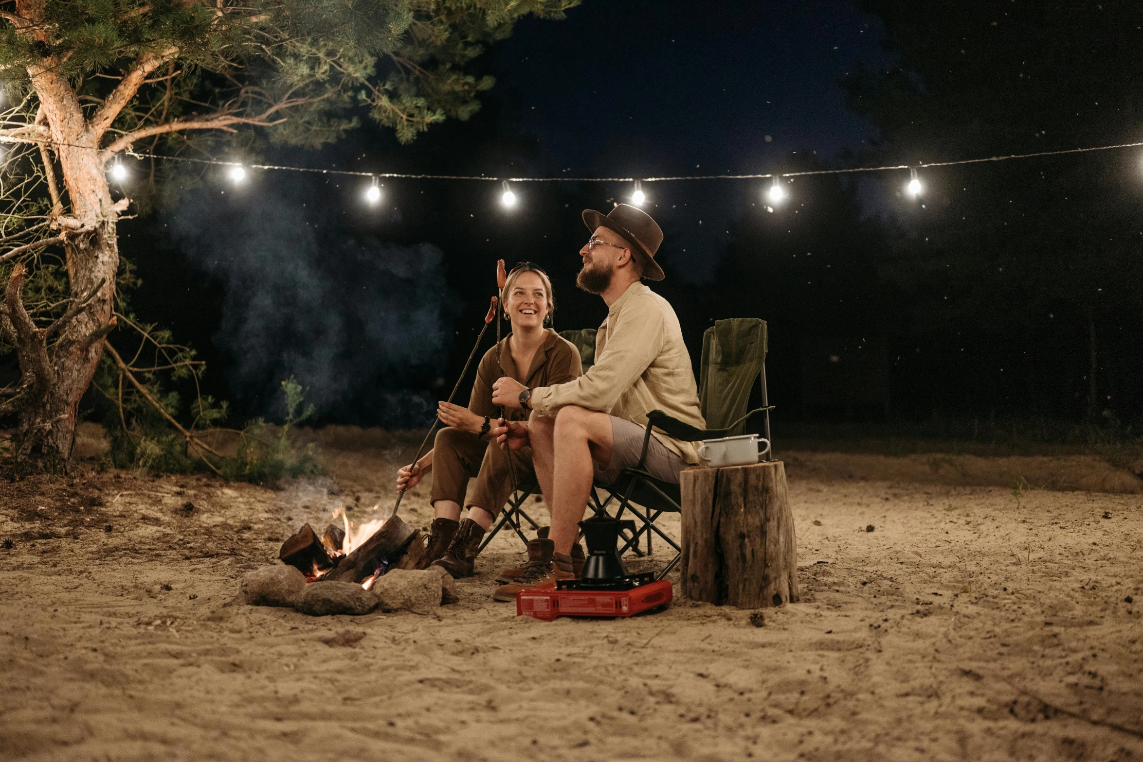 two people sit at a campfire and roast marsh on a night