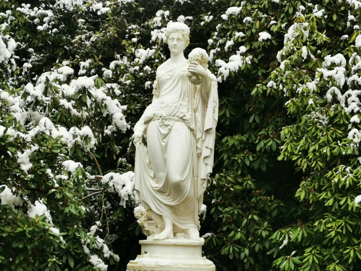 statue of woman standing in garden next to bush and flowers