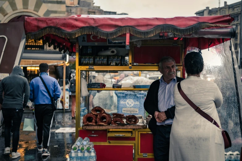 an older woman stands behind a man selling donuts