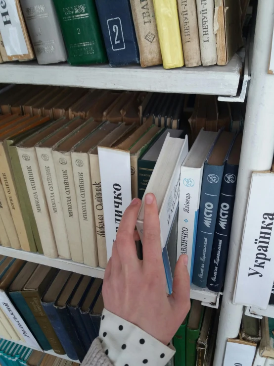 a hand touching a book on top of a shelf in front of a bunch of books