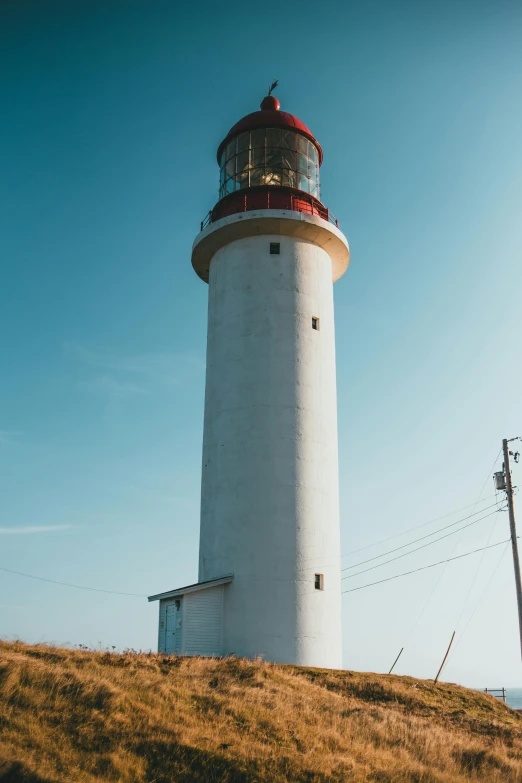 an overcast white lighthouse stands on top of a hill