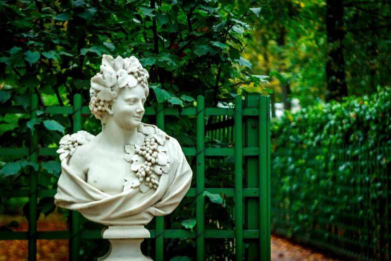 a white statue stands next to a green gate