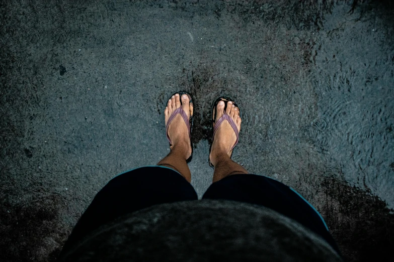 someone wearing slippers is standing near a street with water droplets on them