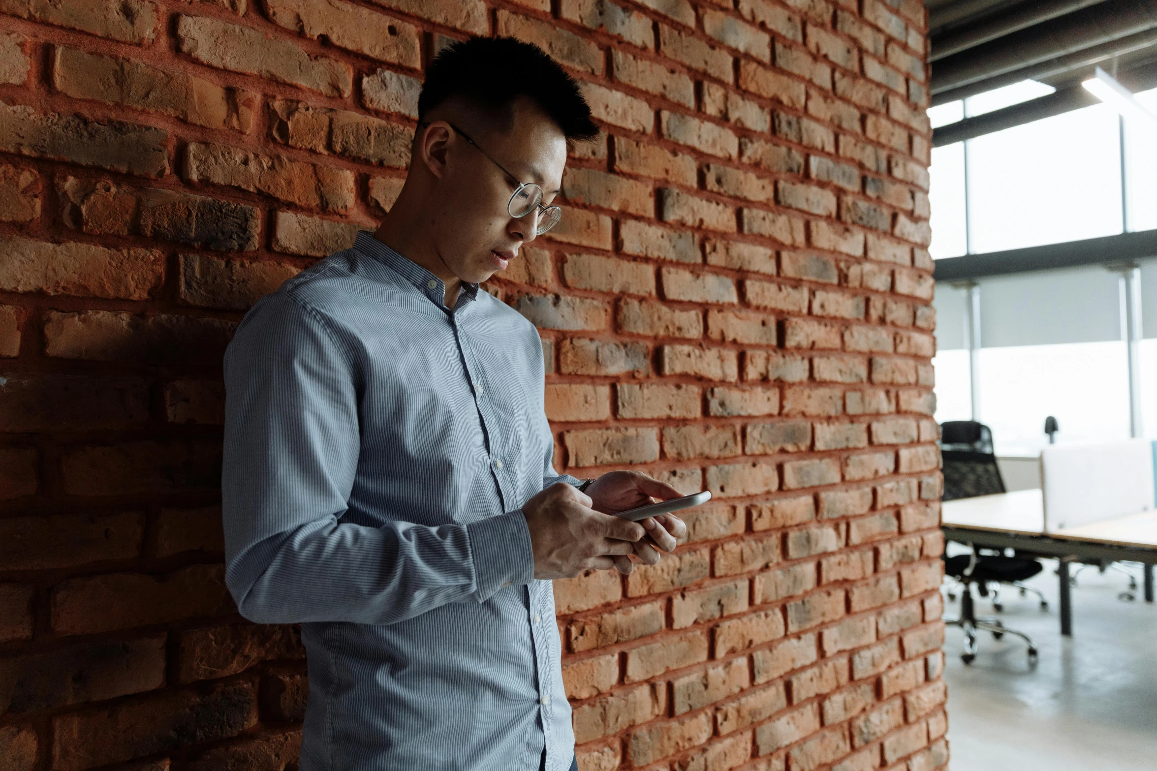 man leaning against a brick wall looking at his cell phone