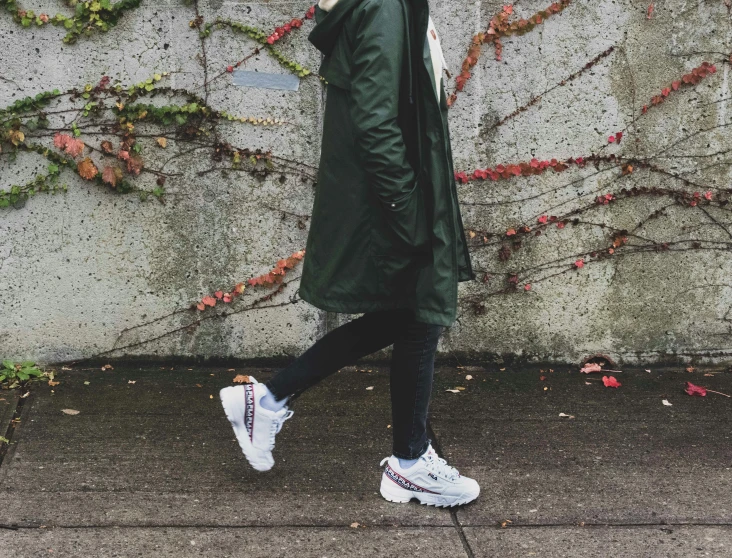 the girl in a green coat is walking by a wall