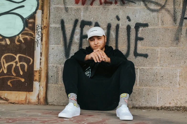 a man sitting against a wall with his hands on his knees