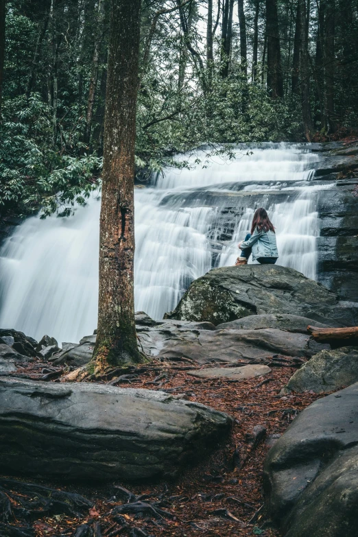 a man with glasses sitting on a rock next to a waterfall
