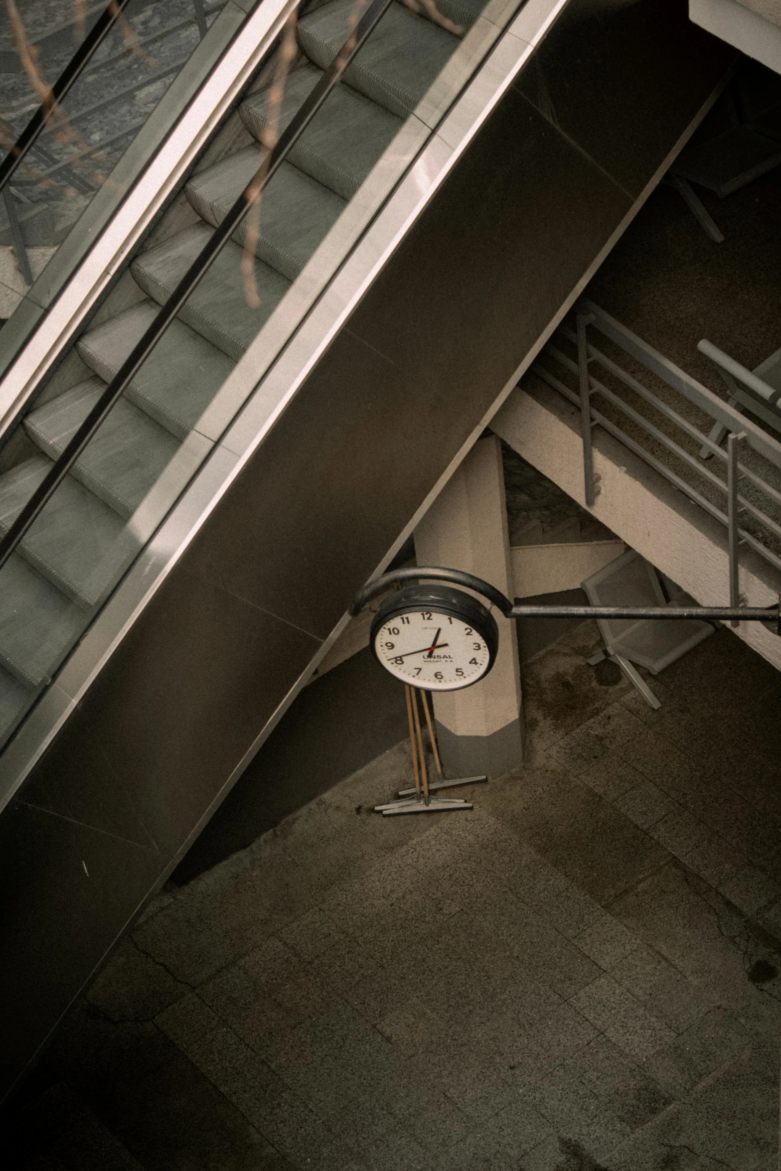 a clock on a pole at the bottom of an escalator