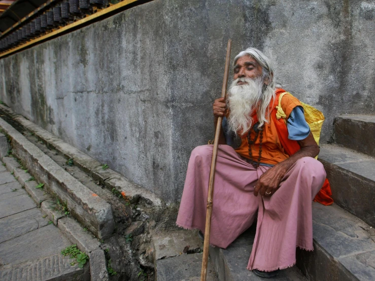 a man with a beard and long white hair sits in front of some stairs