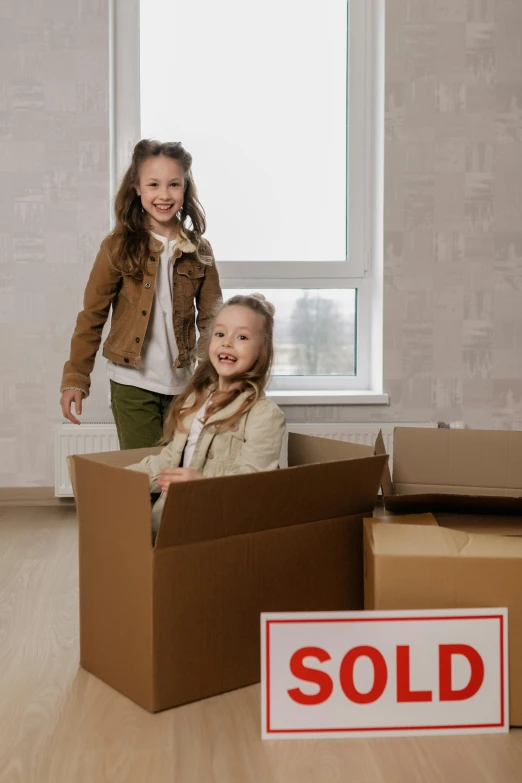 two children standing in a box with sold signs on the floor