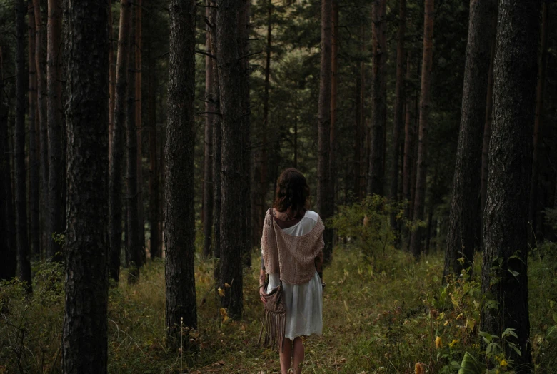 a woman walks through a dark, mysterious forest
