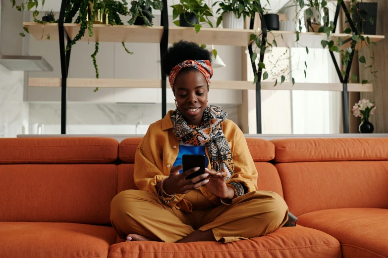 a woman with a turban sits on a couch using her cell phone