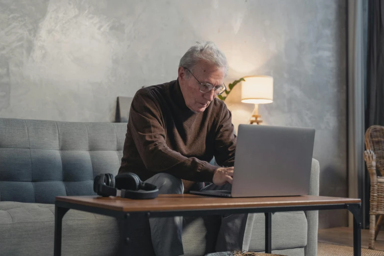 an elderly man uses a laptop on a couch